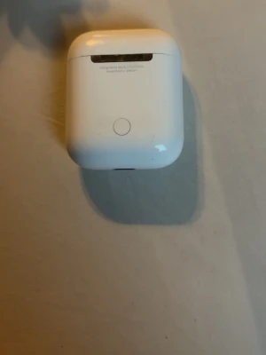 Apple AirPods med vit färg - Säljer ett par vita Apple AirPods med tillhörande laddningsetui. Hörlurarna är trådlösa och har en stilren, minimalistisk design i blank plast. Perfekta för musik, poddar och samtal på språng.