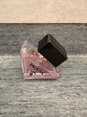 Prada Virtual Flower parfym 30ml - En lyxig parfym från Prada med namnet Virtual Flower. Flaskan är trekantig och gjord av genomskinligt glas med en ljusrosa ton. Locket är stort, svart och fyrkantigt, vilket ger en modern och exklusiv känsla. Perfekt för dig som gillar eleganta och unika dofter.