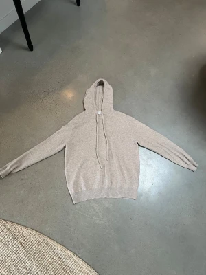 Beige hoodie i mjukt material - Säljer en stilren beige stickad hoodie med huva och dragsnören. Hoodien har en avslappnad passform och är tillverkad i ett mjukt, stickat material som känns skönt mot huden. Perfekt för dig som gillar en clean och enkel look.