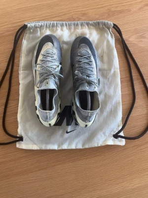 Nike Air Zoom Mercurial fotbollsskor - Säljer ett par Nike Air Zoom Mercurial fotbollsskor i beige och vitt med svarta detaljer. Skorna har hög krage, snörning och mönstrad ovandel i textil för bra passform. Sulan har fasta dobbar för spel på konstgräs primärt. Snygg och modern design, perfekt för dig som vill sticka ut på planen. Hör gärna av dig med prisförslag 