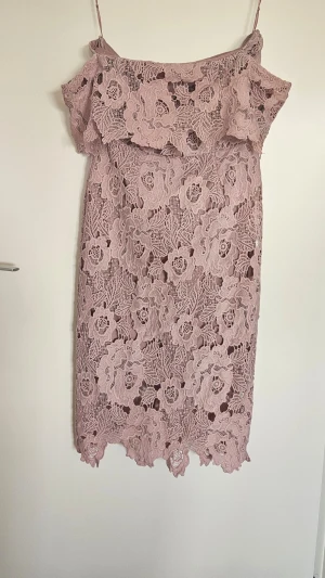 Rosa spetsklänning med volang - Söt rosa kortklänning med blommig spets och volang upptill. Klänningen ät axelbandslös med en romantisk känsla. Perfekt för sommarens tillfällen och har en feminin passform. Använd 1 gång.