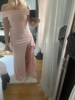 Ljusrosa offshoulder balklänning - Supersnygg ljusrosa långklänning med offshoulder och hög slits. Klänningen har en figurnära passform och markerad. Köpt här på plick men bara testad av mig, använd av hon jag köpte den av en gång på hennes bal, därför smutsig längst ner och har en liten väldigt mild fläck på framsida, se bild 4. Annars i mycket gott skick, bra stretchigt men tjockt material. 
