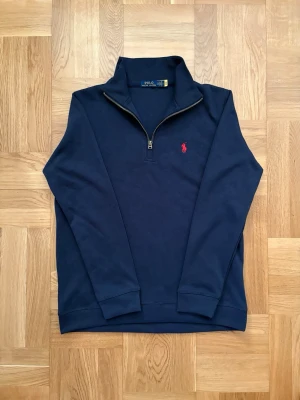     Polo Ralph Lauren tröja half-zip – S, oanvänd - Marinblå half-zip tröja från Polo Ralph Lauren med röd broderad logga på bröstet. Storlek S, helt oanvänd.