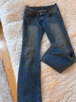 Blå bootcut jeans från Armani - Snygga blå bootcut jeans från Armani med klassisk femficksmodell och broderade loggor på bakfickorna. Jeansen har en lätt tvättad look och är tillverkade i denim med stretch för extra komfort. Perfekta för en trendig och avslappnad stil.