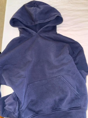 Blå hoodie med mjukisbyxor - En stilren blå hoodie med huva och stor magficka framtill. Tröjan har ribbade muddar vid ärmslut och nederkant med mjukisbyxor. 