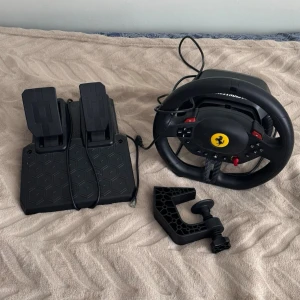 🚗Thrustmaster Ferrari racerratt med pedaler🚗 - Säljer en Thrustmaster racerratt med Ferrari-logga och tillhörande pedaler. Ratten är svart med röda knappar och har flera kontroller för gaming. Pedalerna är också svarta och har en robust design. Perfekt för racing på konsol eller ps. Jag säljer den för jag inte kör ps längre. Tar emot bud. 