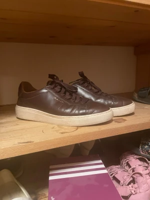 Bruna sneakers från Gant - Snygga bruna sneakers från Gant i läder med vita sulor och matchande bruna skosnören. Klassisk låg modell som passar perfekt till jeans eller chinos. Diskret Gant-logga på sidan och stilren design.