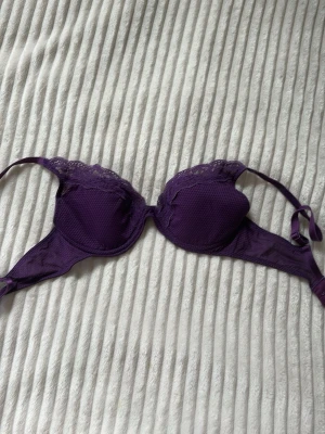 Lila push-up bh med spetsdetaljer - Snygg lila push-up bh med vadderade kupor och fina spetsdetaljer upptill. Justerbara axelband och klassisk knäppning bak. Perfekt för dig som vill ha både komfort och stil. Vet tyvärr inte storleken😅