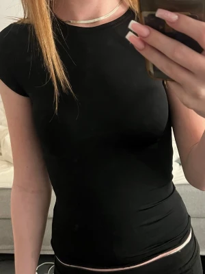 Svart tight t-shirt - En stilren svart t-shirt med tight passform och korta ärmar. Perfekt basplagg som funkar till det mesta och är lätt att matcha. Gjord i mjukt material som sitter skönt mot kroppen.