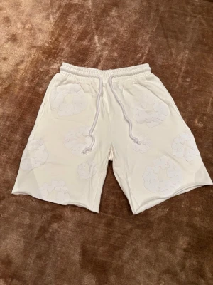 Vita Denim Tears M - Säljer ett par vita Denim Tears med diskret blommönster och snörning i midjan. Shortsen har elastisk midja och en bakficka. Perfekta för sommaren och riktigt sköna att bära till vardags. Pris kan diskuteras. 😊