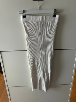 Vit ribbad långkjol Zara - Snygg vit långkjol med ribbad struktur och hög midja. Kjolen är figurnära och har en stilren look som passar perfekt till olika outfits. Materialet är stretchigt och bekvämt, vilket gör den enkel att bära hela dagen. Storleken är M men passar mer som en S