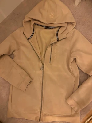Beige hoodie från Sail Racing - Snygg beige hoodie från Sail Racing med dragkedja hela vägen, broderad logga på bröstet och huva med diskret logotyp. Mjuk och skön bomullsblandning, perfekt för chill dagar. Klassisk passform och ribbade muddar vid ärmslut och nederkant.