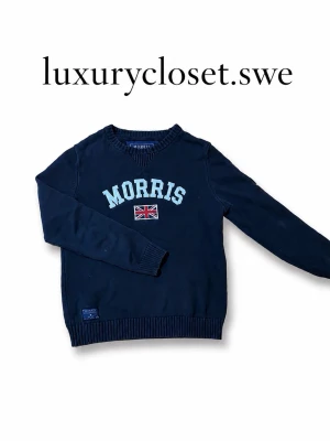 Mörkblå tröja från Morris - Priset kan diskuteras! Mörkblå tröja från Morris storlek mer som S men är också M.Den har rund halsringning och ribbade muddar. Framtill står det 'Morris' i vita bokstäver och under finns en broderad brittisk flagga. Tröjan har en klassisk passform, passar perfekt till dem som är 155-175cm och är perfekt för en stilren look.
