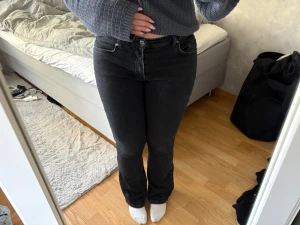 Svarta bootcut jeans med låg midja  - Säljer ett par svarta bootcut jeans med låg midja och klassisk femficksdesign. Jeansen har en snygg passform som sitter tajt över låren och släpper ut vid bensluten. Perfekta till en stickad tröja eller t-shirt.