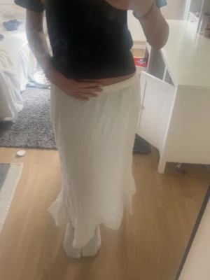 Vit långkjol från Vero Moda - Säljer en vit lågmidjad långkjol från Vero Moda med lätt skrynklig struktur och flowig passform. Är perfekt för en avslappnad och stilren look. Insydd i midjan så passar mig som har xs/s!