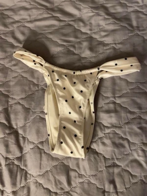 Prickiga bikini underdel med knyt i sidorna - Snygga underdel  med svarta prickar och knyt i sidorna. Underdelen har en klassisk bikini-modell och är tillverkade i ett mjukt och stretchigt material som känns bekvämt mot huden. 