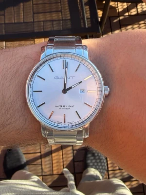 Silverfärgad klocka från GANT - Stilren klocka från GANT i silverfärgat rostfritt stål med klassisk rund urtavla och datumvisning. Urtavlan är ljus med minimalistiska markeringar och armbandet är länkformat i metall. Perfekt accessoar för en clean look.