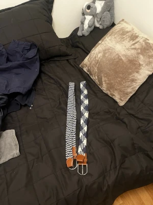 Två mönstrade bälten med läderdetaljer - Två snygga bälten i blått och vitt med olika mönster, båda har bruna läderdetaljer vid spännet och ändarna. Bältena har ett coolt, randigt och grafiskt mönster som sticker ut och passar perfekt till jeans eller chinos.