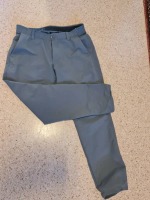 Golf byxor från under armour - Snygga och stilrena golfbyxor från Under Armour i en modern blågrå nyans. Byxorna kombinerar en sportig känsla med en stilren passform, vilket gör dem perfekta både på golfbanan och till en casual vardagslook. Det lätta och stretchiga materialet ger hög komfort och full rörelsefrihet under hela dagen. Perfekta för dig som vill ha ett par funktionella och samtidigt riktigt stilrena byxor med premiumkänsla. Diskret design som enkelt matchas med både piké och hoodie.