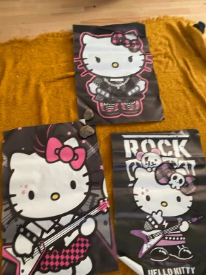 Hello Kitty rockiga posters - Tre coola Hello Kitty-posters med rocktema. Motiven visar Hello Kitty med elgitarr, dödskalleaccessoarer och rutiga detaljer i svart, vitt och rosa. Perfekt för att piffa upp rummet med en unik och lekfull stil.