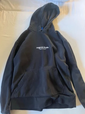 Svart hoodie från Originals Studio - Svart hoodie från Originals Studio med vit logga tryckt på bröstet. Bra i skick och inte använd mycket.