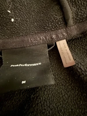Svart fleece från Peak Performance - Mysig svart fleecejacka från Peak Performance i storlek M. Tillverkad i mjukt fleecematerial som håller dig varm. Perfekt för lager-på-lager och har en klassisk, enkel design utan synliga detaljer.