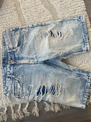Ljusblå  jeansshorts  - Säljer ett par ljusblå jeansshorts från FSBN med snygga slitningar och råa detaljer framtill. Klassisk femficksmodell med knapp och dragkedja. Perfekta för en avslappnad och trendig look. Jag har sällan använt dem och vill Darför sälja dem