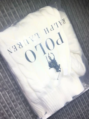 Vit kabelstickad tröja Polo Ralph Lauren - Vit kabelstickad tröja från Polo Ralph Lauren med halv dragkedja och broderad logga på bröstet. Tröjan har ribbstickad krage och muddar, perfekt för en clean och klassisk look.
