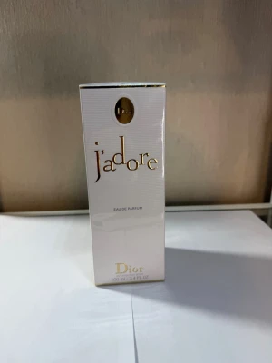 J'adore Eau de Parfum från Dior - J'adore Eau de Parfum från Dior i en elegant vit och guldig förpackning. Flaskan rymmer 100 ml och doften är känd för sin lyxiga och blommiga karaktär. Perfekt för dig som vill ha en ikonisk och tidlös parfym från ett exklusivt märke.