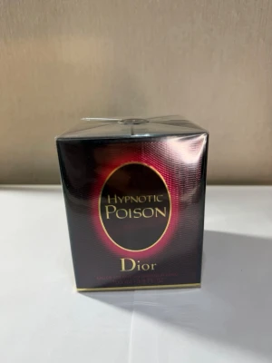Dior Hypnotic Poison Eau de Toilette - Dior Hypnotic Poison Eau de Toilette i en elegant svart och röd kartong med guldiga detaljer. Parfymen är känd för sin sensuella och mystiska doft, perfekt för dig som gillar lyxiga och ikoniska parfymer. Förpackningen är fyrkantig och har en exklusiv känsla.