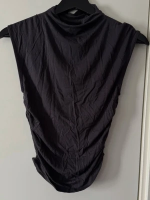 Svart ärmlös polotopp från Gina Tricot - Svart ärmlös polotopp i mjukt och stretchigt material från Gina Tricot. Toppen har en hög krage och en figurnära passform som ger en stilren och modern look. Perfekt att matcha med jeans eller kjol för en trendig outfit.