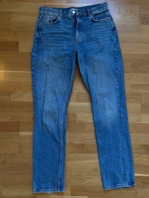 Blå raka jeans från Gina Tricot - Klassiska blå jeans från Gina Tricot i rak modell med fem fickor och normal midja. Jeansen har en snygg tvättad look och stängs med dragkedja och knapp. Perfekta för en avslappnad och trendig stil.