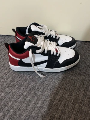 Nike Air Jordan 1 Low svart/vit/röd - Snygga Nike Air Jordan 1 Low sneakers i svart, vitt och rött läder. Klassisk låg modell med vit tåbox, svarta detaljer och röd häl. Ikonisk Jumpman-logga på plösen och svart Swoosh på sidan. Perfekta för dig som gillar streetstyle och basketinspirerad design.