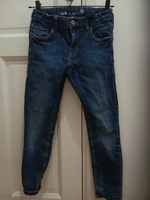 Mörkblå jeans i barnstorlek - Jeansen är i gott skick, de enda tecken på använding är lite smuts på botten och något slitet tyg på fickor och byxbotten. Elastisk remm.