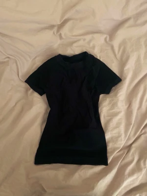Svart topp/träningstopp - Säljer en svart, tight topp med korta ärmar och rund hals. Man kan ha den till träning eller samt som basplagg. Materialet är dock träningsmaterial. Den är i storlek S men hade nog passat xs också då den är tight❤️ 