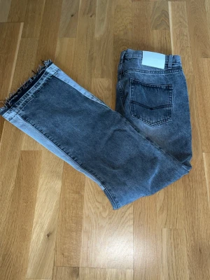 Gråa flared jeans från gallery dept - Säljer ett par grå jeans från gallery dept med cool tvåfärgad design och raka ben. Jeansen har ljusare paneler längs sidorna och råa, fransiga benslut. Klassisk femficksmodell och knappgylf. Perfekta för en trendig streetstyle-look.