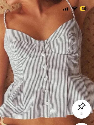 Randig korsettopp med knappar - Snygg randig korsettopp med tunna axelband och knappar framtill. Toppen har en figurnära passform upptill och lätt utsvängd nertill. Perfekt för en trendig och somrig look.