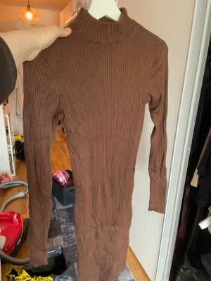 Brun ribbad långärmad klänning - Säljer en brun ribbad klänning med lång ärm och hög krage. Klänningen är figurnära och har en enkel, stilren design som passar perfekt till många olika tillfällen. Materialet är mjukt och stretchigt för en bekväm passform.