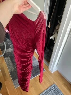 Röd långärmad meshklänning - Snygg röd långärmad klänning i mesh med rynkade detaljer längs sidorna. Klänningen har en kroppsnära passform och är perfekt för dig som vill sticka ut. Materialet är lätt och stretchigt, vilket gör den bekväm att bära.