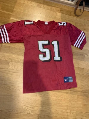 Röd NFL-tröja Reebok  - Snygg röd NFL-tröja från Reebok med nummer 51 och namnet Norton på ryggen. V-ringning