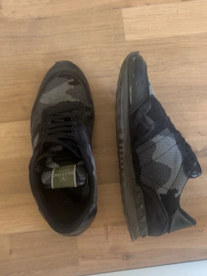 Valentino camo rockrunners i svart och grått - kom med bud!                                                   Snygga sneakers från Valentino med svart och grått camouflagemönster. Skorna har svarta snören, meshdetaljer och partier i mocka. Klassisk låg modell med robust sula och diskret logga på plösen. Perfekta för dig som gillar streetstyle och exklusiva märken.