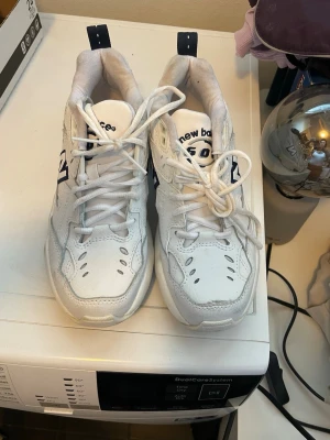 Vita New Balance 530 sneakers - Säljer ett par vita New Balance 530 sneakers med marinblå detaljer och klassisk N-logga på sidan. Skorna har chunky sula, ventilerande meshpartier och är tillverkade i en mix av läder och syntet. Perfekta för en sportig och trendig look.