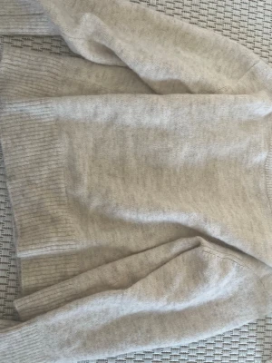 Beige stickad tröja från Gina Tricot - Mysig beige stickad tröja från Gina Tricot med ribbade muddar vid ärmslut och nederkant. Tröjan har en klassisk rund halsringning och är tillverkad i ett mjukt, fluffigt material som passar perfekt för kyligare dagar.