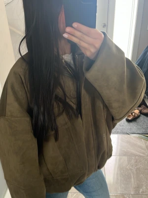 Oversized grön bomberjacka i mocka-look - Snygg oversized bomberjacka i grön mocka-look med dragkedja framtill och stora fickor på sidorna. Jackan har bred krage och långa ärmar med avslappnad passform. Perfekt för dig som gillar streetstyle och vill ha en trendig jacka till din outfit. Den är från Zara och är köpt i Frankrike.
