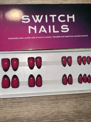 Switch Nails Velvet Aura Almond Short - Press-on naglar i färgen Velvet Aura från Switch Nails. Naglarna har en snygg ombre-effekt i mörkrött och svart, med kort mandelform. Tillverkade av återvunnet material och kan återanvändas. Perfekt för dig som vill ha salongskänsla hemma. Säljes utan tillbehör