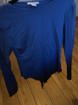 Blå långärmad body från Samsoe Samsoe - Snygg blå body med långa ärmar från Samsoe Samsoe. Modellen har rund halsringning och är tillverkad i ett stretchigt, mjukt material som sitter skönt mot kroppen. Perfekt att styla med jeans eller kjol för en trendig look.