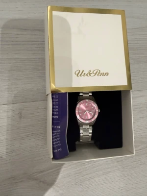 Silverfärgad klocka med rosa urtavla - Stilren klocka från Ur & Penn med silverfärgad länk och en snygg rosa urtavla. Klockan har klassisk rund form och levereras i originalask. Perfekt accessoar för att lyfta din outfit.
