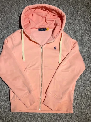 Rosa hoodie från Polo Ralph Lauren XS - Snygg rosa hoodie från Polo Ralph Lauren med dragkedja och huva. Klassisk logga broderad på bröstet och vita snören i huvan. Perfekt för en avslappnad och trendig stil. Storlek och mått kan informeras privat. Pris kan Diskuteras. 😊