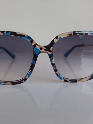 Fyrkantiga leopardmönstrade solglasögon - Snygga solglasögon med fyrkantiga bågar i leopardmönster med inslag av blått, beige och svart. Glasen är tonade och ger en cool vibe till din stil. Perfekta för dig som vill sticka ut och addera färg till din look.