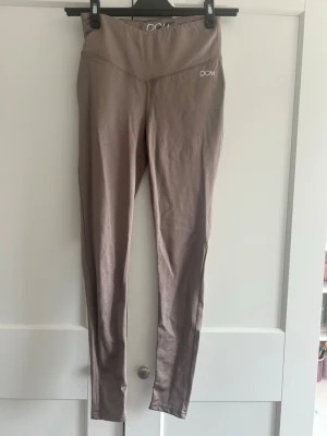 Mauve leggings från DOM - Snygga mauvefärgade tränings byxor från DOM med hög midja och diskret logga framtill. Stretchigt och mjukt material som sitter skönt på kroppen. Perfekta till träning eller chill. Snygg sömdetalj över höfterna för extra stilpoäng.